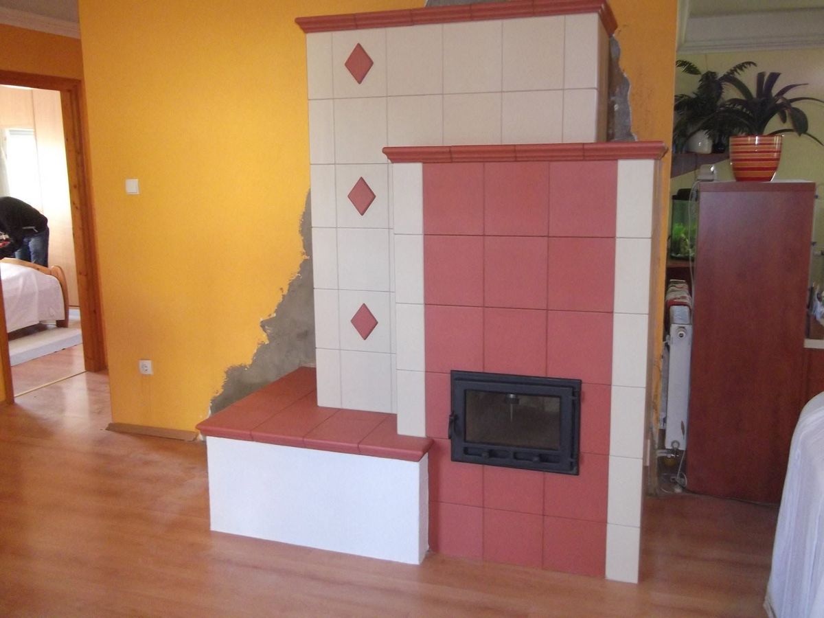 Fehér és terrakotta színű csempékből kialakított kályha, egyenes vonalakkal és sötét üveges ajtóval.